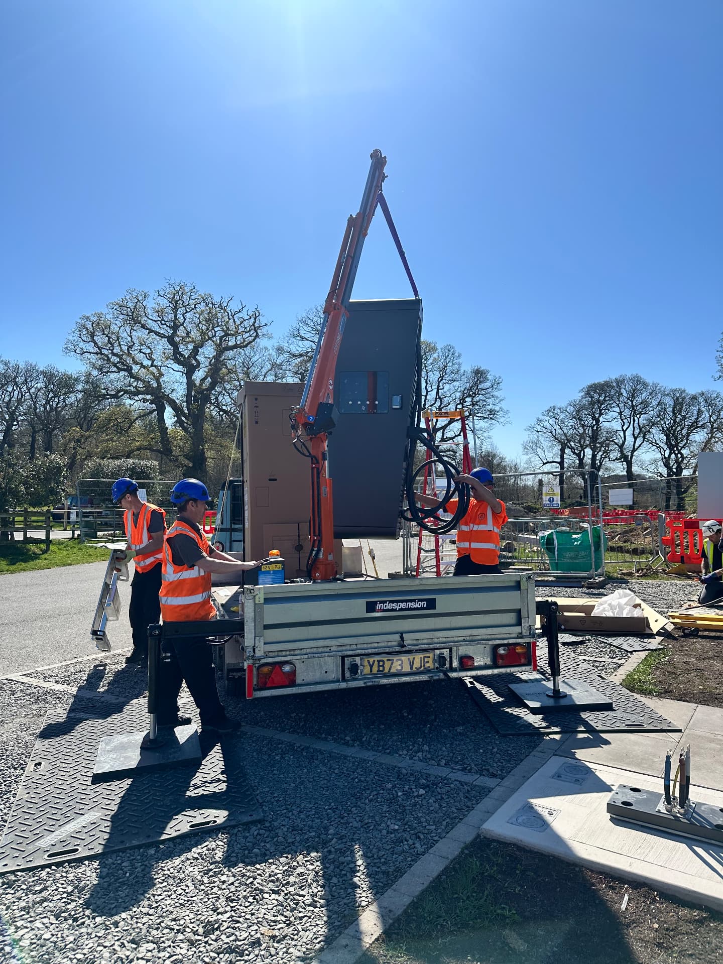Crew offloading an EV charger from a HIAB trailer onto ground protection mats