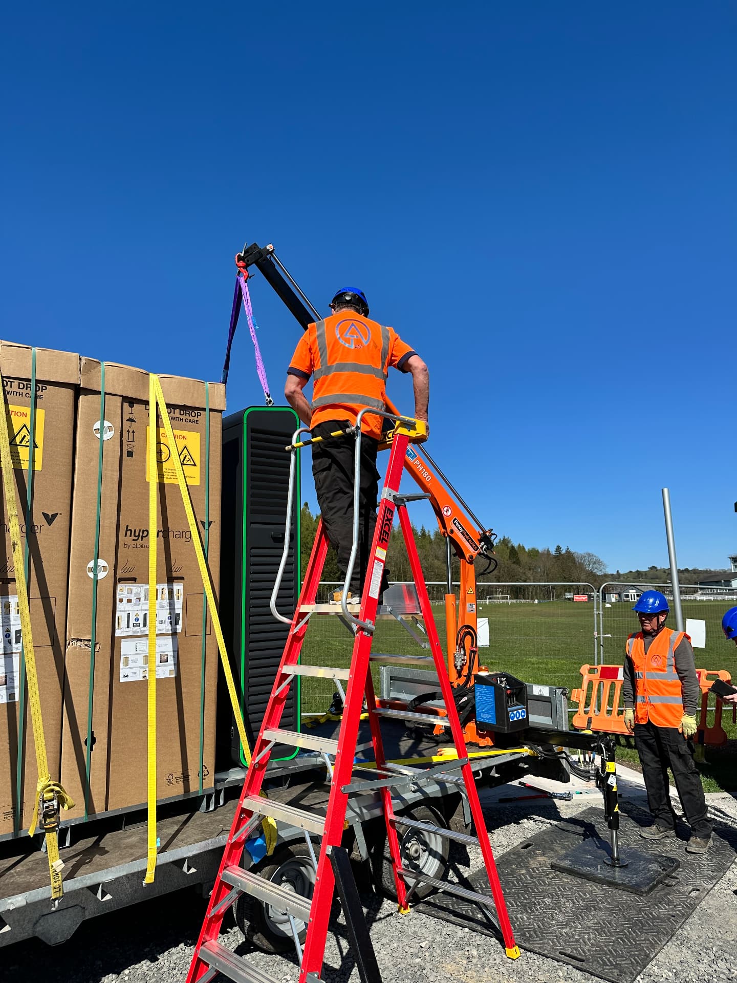 Operative on a podium step rigging an EV charger to a trailer-mounted HIAB