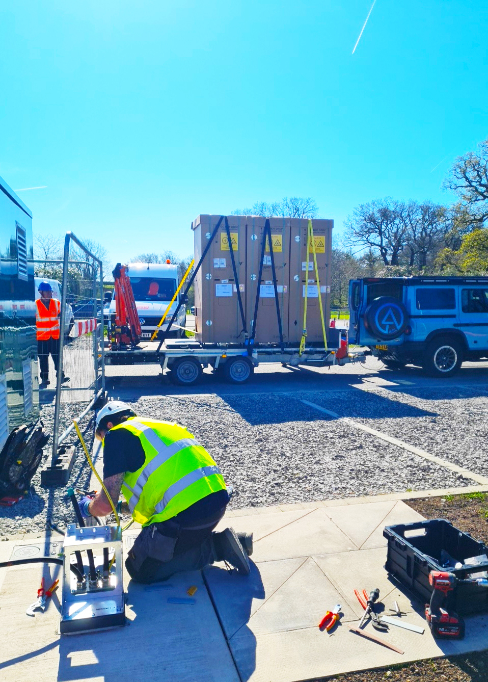 Operative preparing an installation while crated EV cabinets sit strapped on a trailer