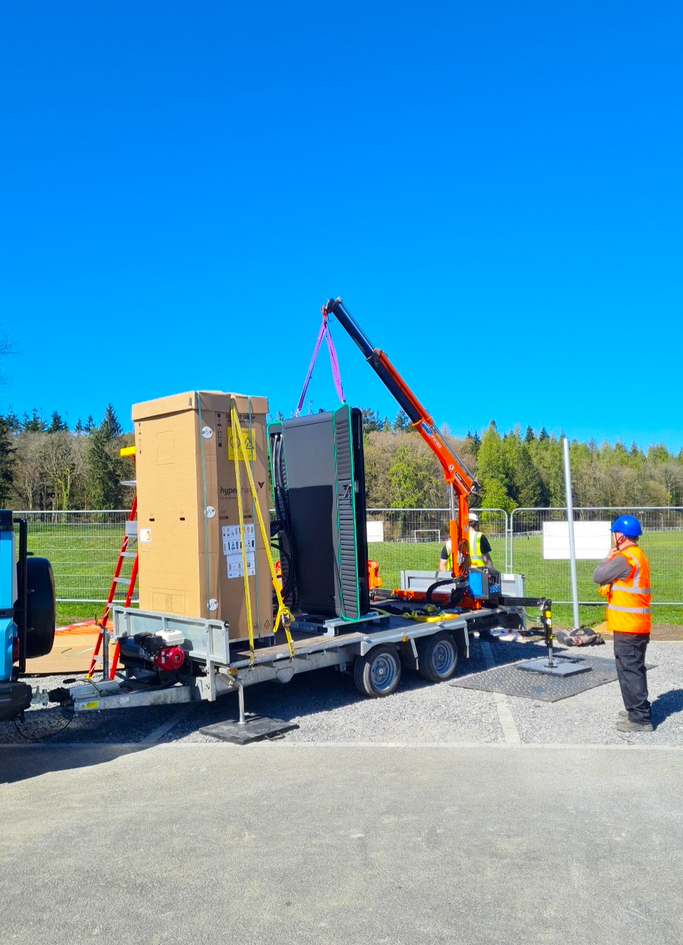 Crew using a HIAB to lift an EV rapid charger from a trailer